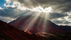 Rayos de sol atravesando nubes sobre una montaña roja creando una iluminación dramática