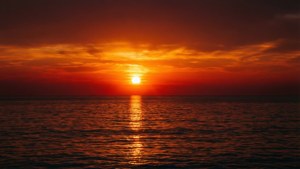 Un atardecer simétrico sobre el mar con reflejos anaranjados y rojos. — Vista del cielo Fondos de pantalla