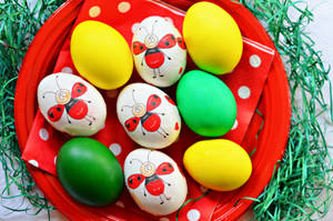 Huevos de Pascua pintados de amarillo, verde y con dibujo de mariquita en un plato rojo, fondo de Pascua