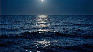 Olas calmadas de océano azul oscuro bajo la luz de la luna, ideal para un fondo de pantalla estético y pacífico.