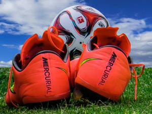 Fondo de pantalla de escritorio de tacos de fútbol, balón de fútbol y campo verde.