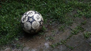 Fondo de pantalla de escritorio de balón de fútbol embarrado en un charco con césped verde.