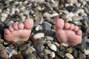 Pies sobre las rocas durante las vacaciones de verano, situación divertida en la playa con guijarros.